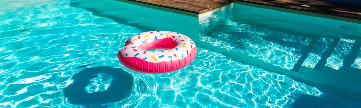 Pink donut inflatable float in turquoise swimming pool with shadow, wooden deck, and submerged steps