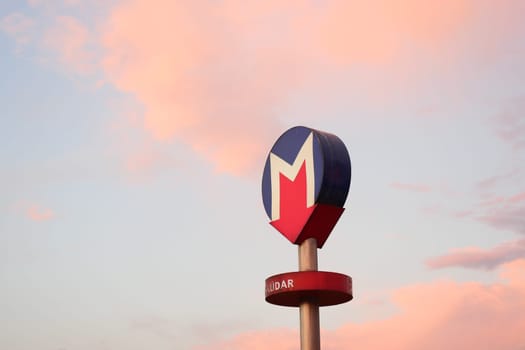 A subway station sign stands tall with a pastel sky at dusk.