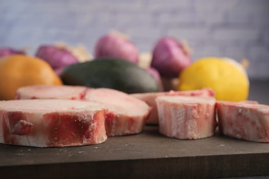 A wooden board displays freshly sliced meat next to vibrant vegetables.