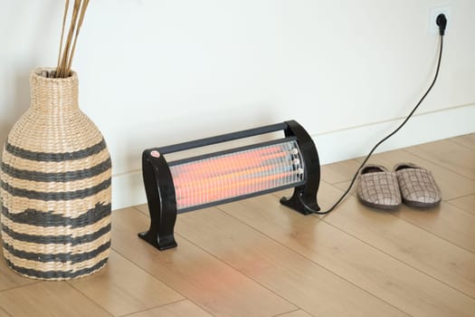 A stylish heater warms the room beside a woven basket and slippers.