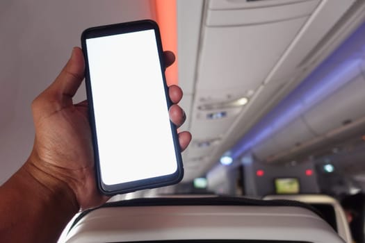 A person holds a blank smartphone inside an airplane cabin during flight.