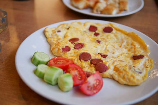 Omelet with sliced sausage served with fresh tomato and cucumber slices.