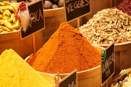 Piles of vibrant spices are arranged in wooden containers at a market.