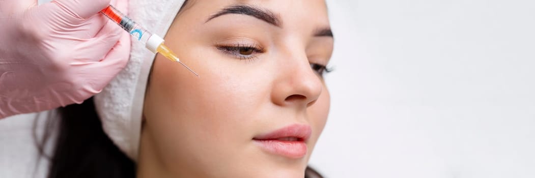 Cosmetologist makes rejuvenating anti wrinkle injections on the face of a beautiful woman. Female aesthetic cosmetology in a beauty salon
