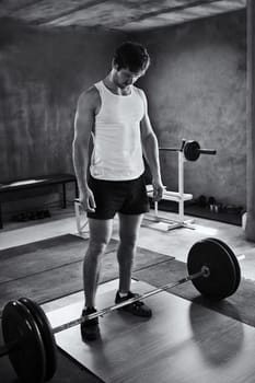 Black and white image of a strong young man looking quietly at the weights he is about to lift