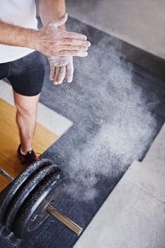 High angle view of a man dusting his hands with powder with the weight he's about to lift at his feet