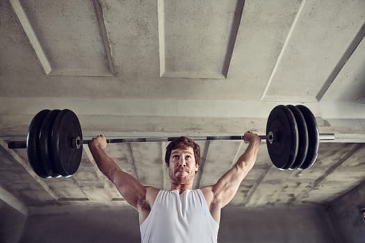 Low angle shot of a strong young man lifting heavy weigths above his head with a determined expression