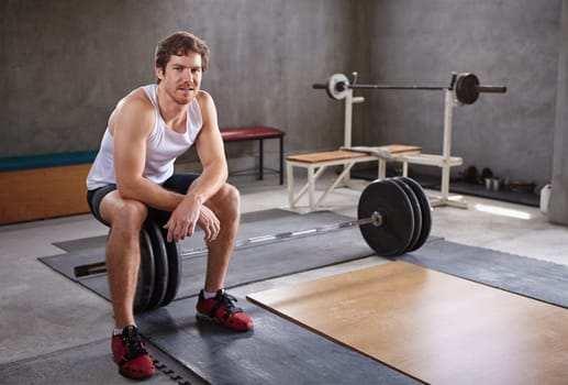 Handsome young man sitting on wieghts looking at the camera in a private gym