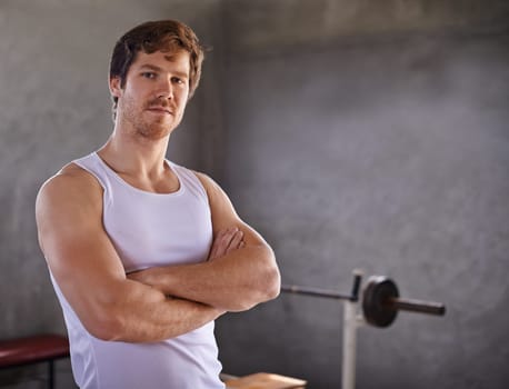 Handsome young man with strong physique looking confidently at the camera with weigthlifting equipment in the background