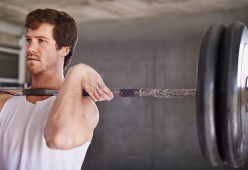 Handsome young man with strong physique lifting heavy weights in a private gym
