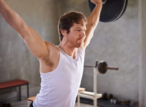 Strong man looking fiercely determined while lifting heavy weights in a private gym
