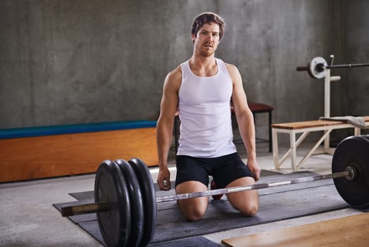 Fit personal trainer kneeling behind his weightlifting equipment in a private gym