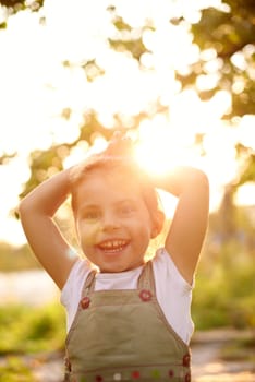 Cute little girl outside smiling happily with early morning sunlight filtering through the trees