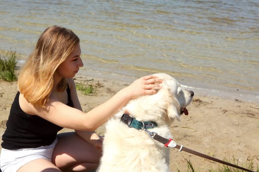 A young girl delights in a beautiful sunny day by the water, happily petting her friendly golden retriever companion