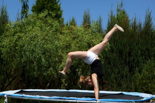 A young girl joyfully displays her acrobatic skills on a trampoline, surrounded by vibrant lush greenery