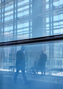 Blue tone images of real businesspeople in motion through glass in a busy conference centre