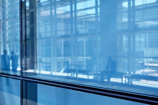 Blue tone images of real businesspeople in motion through glass in a busy conference centre