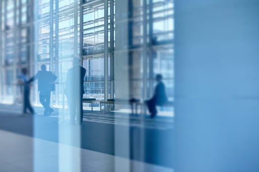 Blue tone images of real businesspeople in motion through glass in a busy conference centre
