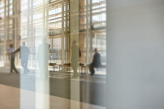 Abstract images of real businesspeople in motion through glass in a busy conference centre