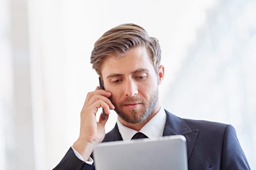 Closeup of a serious corporate executive listening on his phone while looking at a digital tablet