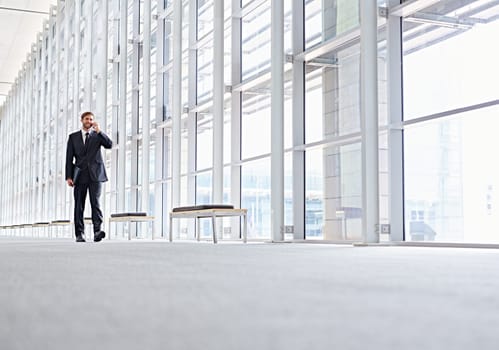Low angle shot of a corporate executive walking along a modern corridor talking on his mobile phone