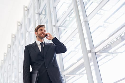 Low angle shot of a corporate executive walking along a modern corridor talking on his mobile phone