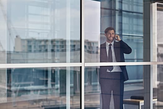 A happy businessman looking out the window while talking on his cellphone