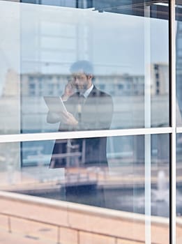 View through a window of a corporate executive talking on his phone and looking at a digital tablet