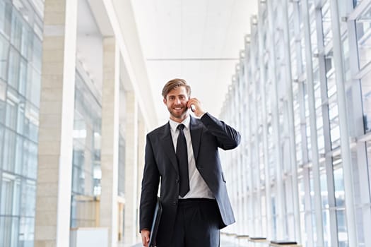 Corporate executive smiling at the camera while talking on his phone and walking down a corridor