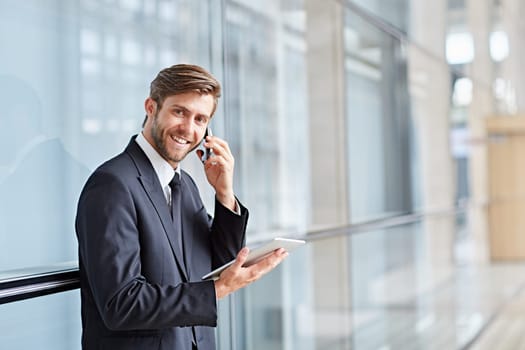 Portrait of a corporate executive smiling while talking on his phone and holding at a digital tablet