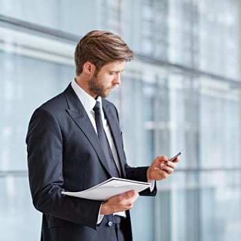 Corporate executive using his cell phone in a modern architectural setting while holding notes