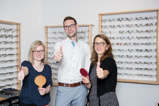 in optician shop- two women and one man with thumb up selecting new glasses