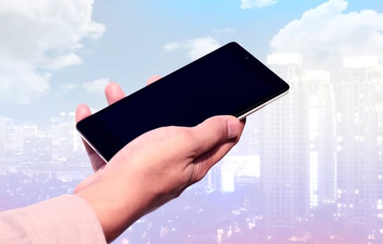 Hand holding cellphone with blank screen on cityscape background. You can put your design on the cellphone