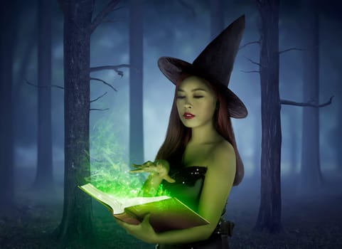 Beautiful asian girl wearing witch cloth reading spell in the book on the forest at night