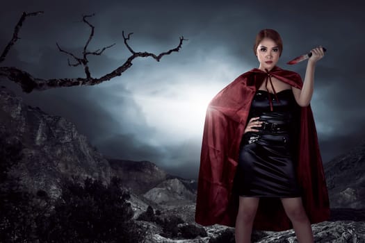 Beautiful asian witch woman holding bloody knife in the night, horror situation. Halloween concept image