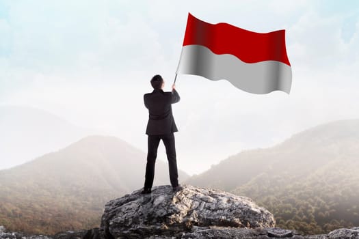 Successful man waving Indonesian flag on top of the mountain peak