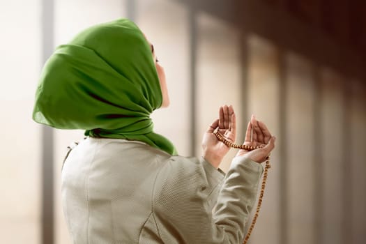 Young muslim woman holding prayer beads over mosque background