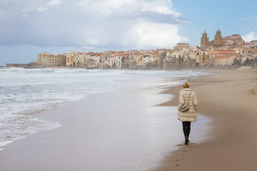 Solitary woman walking empty beach of Cefalu in winter time, Sicily, south Italy.