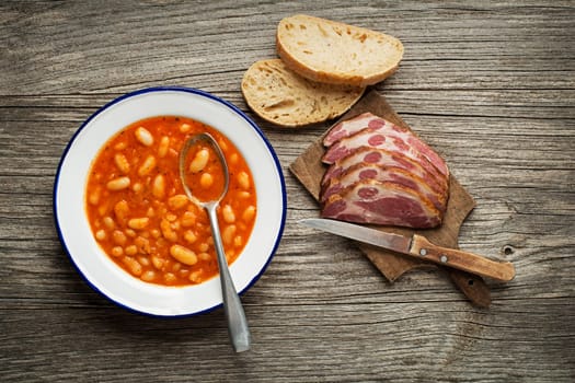 White bean stew with tomato sauce and meat on wooden table