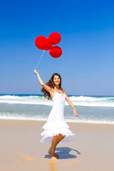Beautiful girl running in the beach with red ballons in her hand