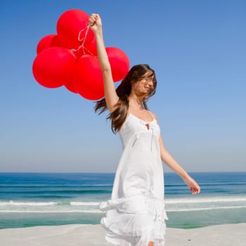 Beautiful girl running in the beach with red ballons in her hand