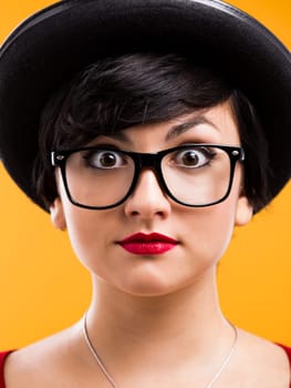 Beautiful nerd girl wearing a santa hat and holding a gift, against yellow background