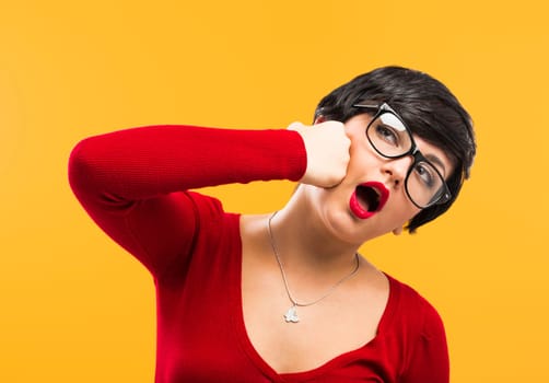 Beautiful nerd girl wearing a santa hat and holding a gift, against yellow background