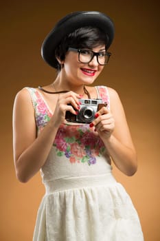 Vintage girl taking pictures using an old camera in a beige background