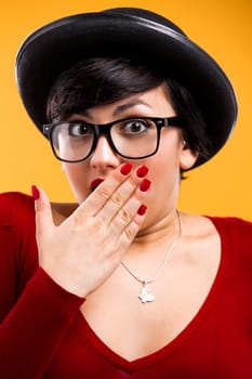 Beautiful nerd girl wearing a santa hat and holding a gift, against yellow background