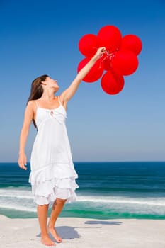Beautiful girl running in the beach with red ballons in her hand