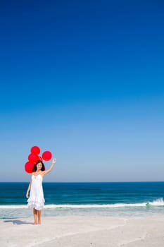 Beautiful girl running in the beach with red ballons in her hand