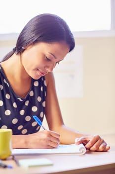A young woman writing while sitting in her office