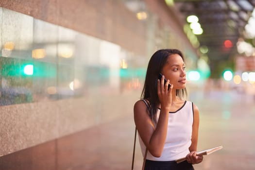 A young businesswoman talking on her phone while standing in front of an office block
