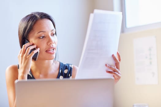 A young businesswoman talking on the phone while looking at a document